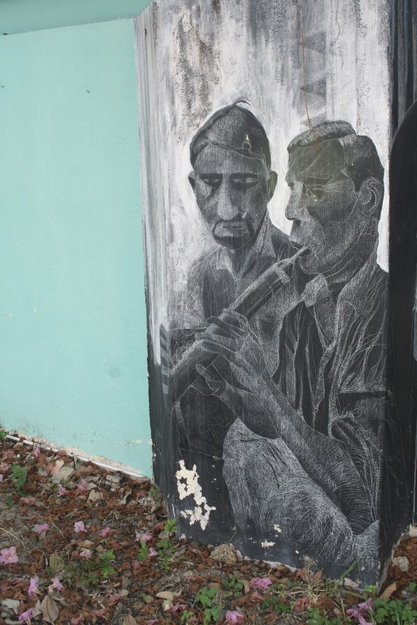 A charcoal mural of two men in caps painted on a wall above wild flowers