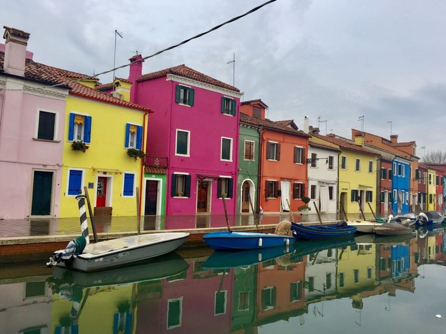 Brightly painted canal houses reflected in still water, with moored boats
