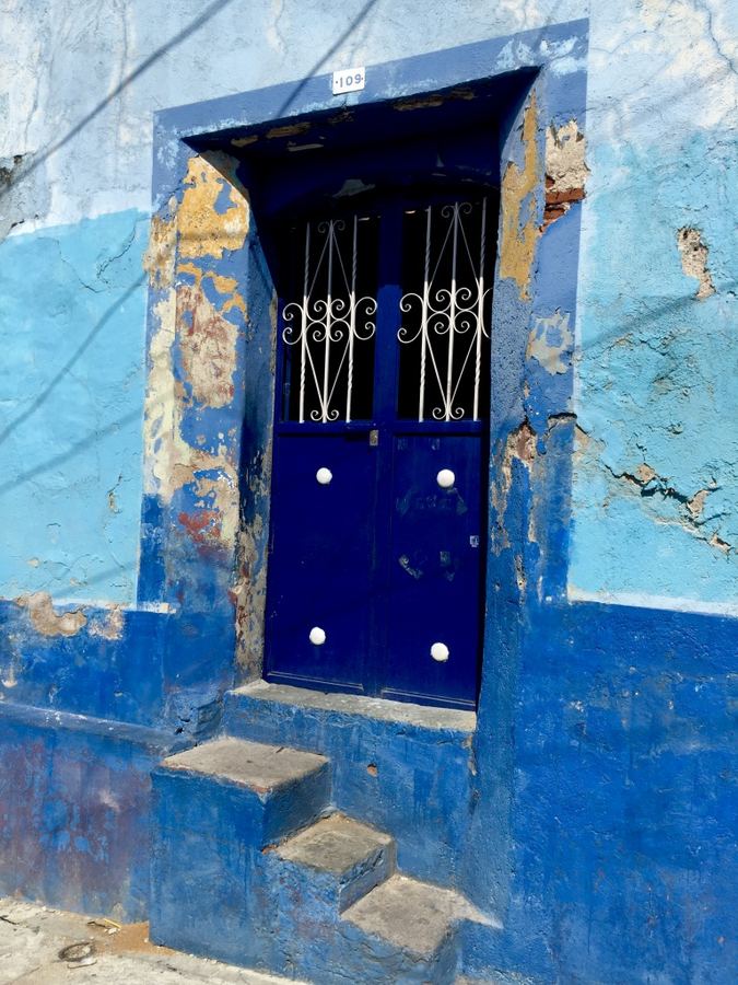 A deep blue door and worn steps set into a painted blue wall