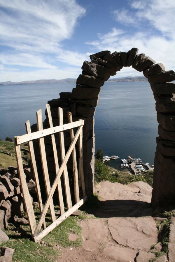 A dry-stone arch and wooden gate framing a lake far below