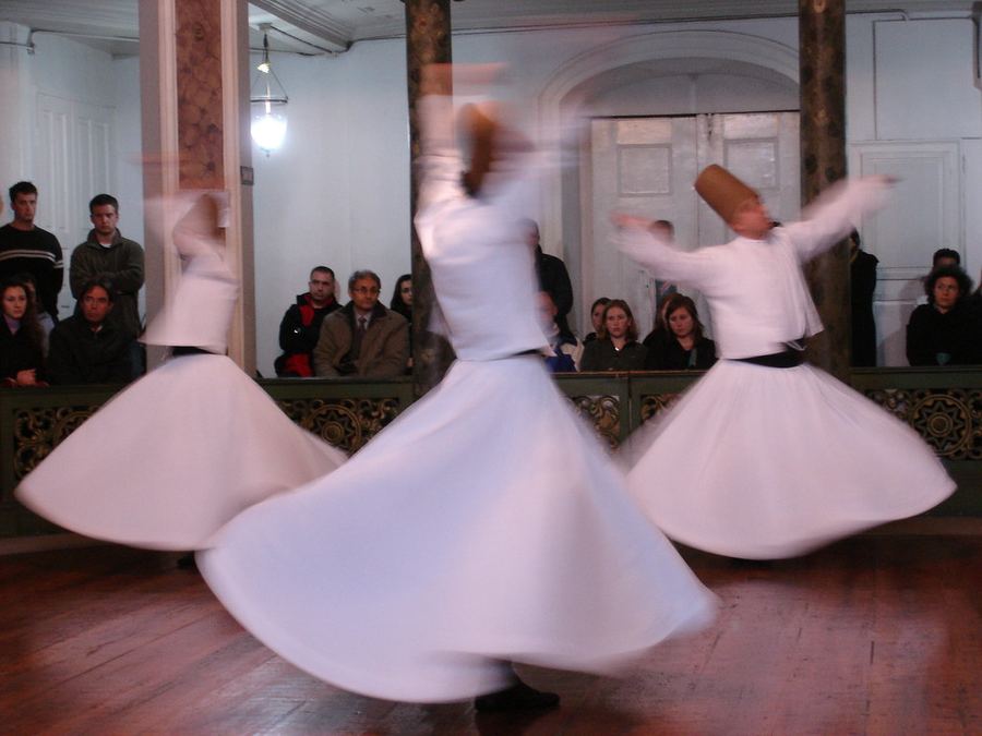 Whirling dervishes turning in white robes before a seated audience