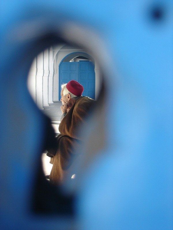 A man in a red fez seen through a keyhole-shaped opening