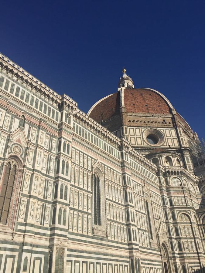 The striped marble facade and dome of Florence cathedral against a deep blue sky