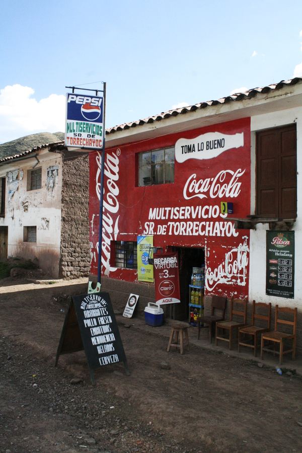 A corner shop painted in Coca-Cola red beneath a Peruvian hillside