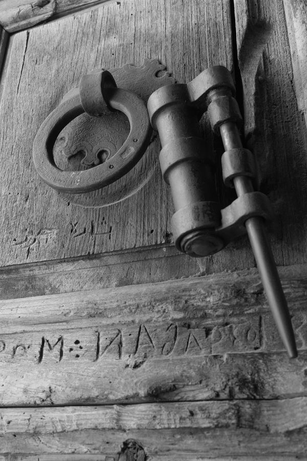 A wrought-iron latch and ring handle on a weathered carved door