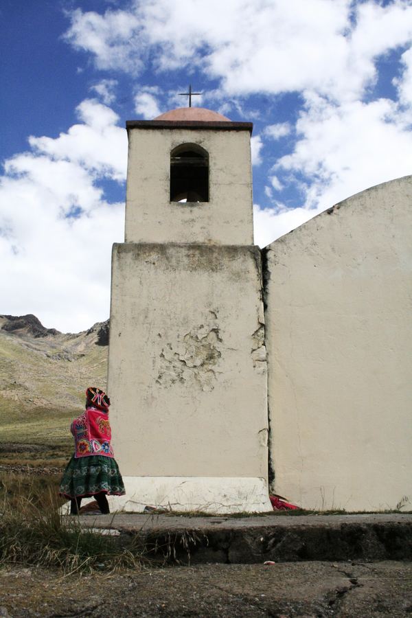 A whitewashed chapel with a figure seated at its base