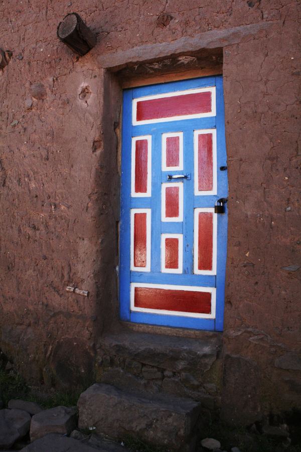A blue and red painted door set into a red earthen wall