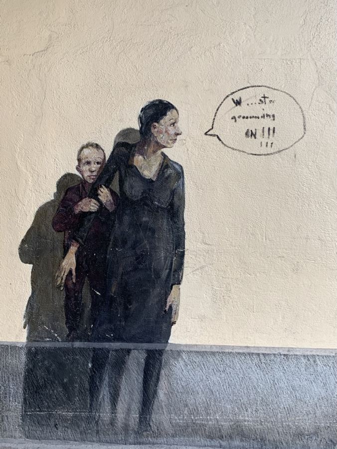 A mural of a woman and child on a pale wall beside a painted speech bubble