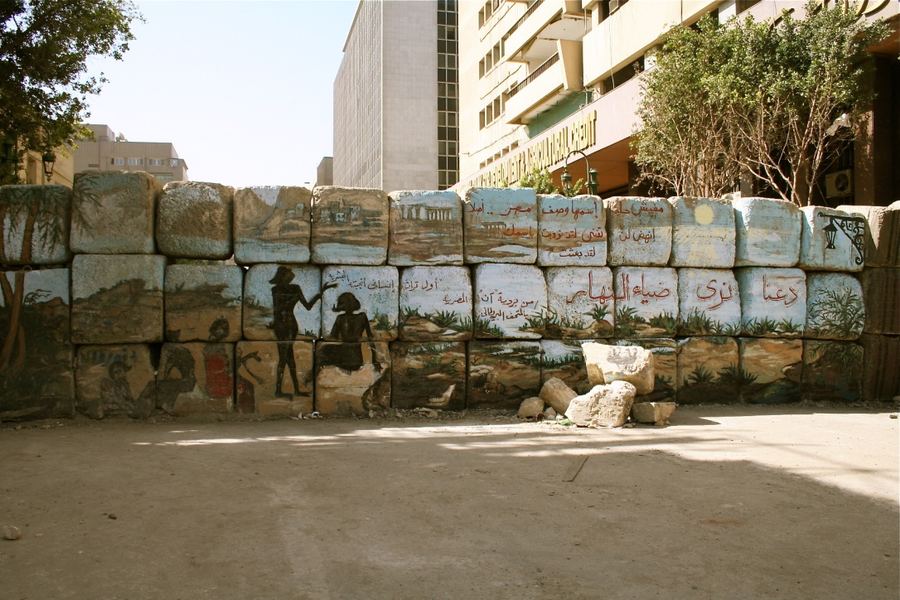 A concrete blast wall painted with a mural of figures and Arabic script