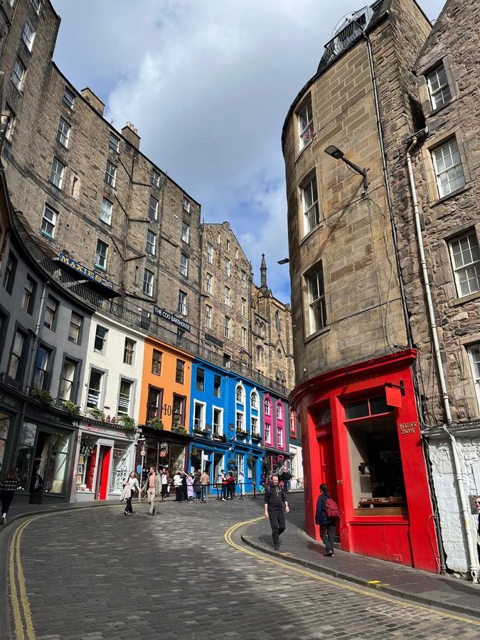 A curving cobbled street of tenements above brightly painted shopfronts
