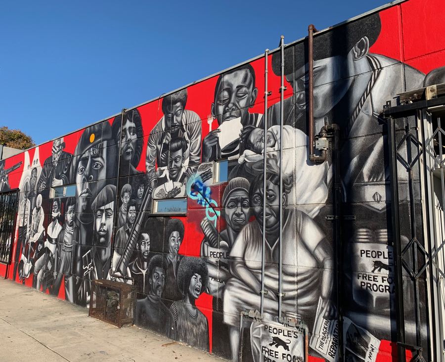 A mural of massed faces in red, black, and white along a city wall