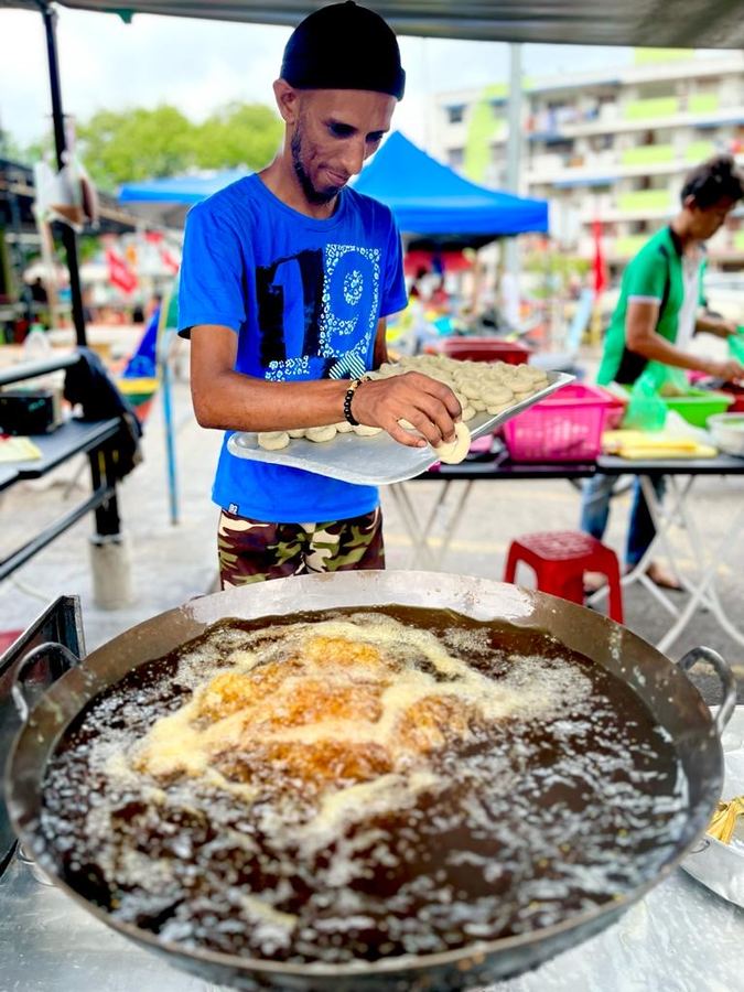 A street vendor frying pastries in a wide pan at a market stall