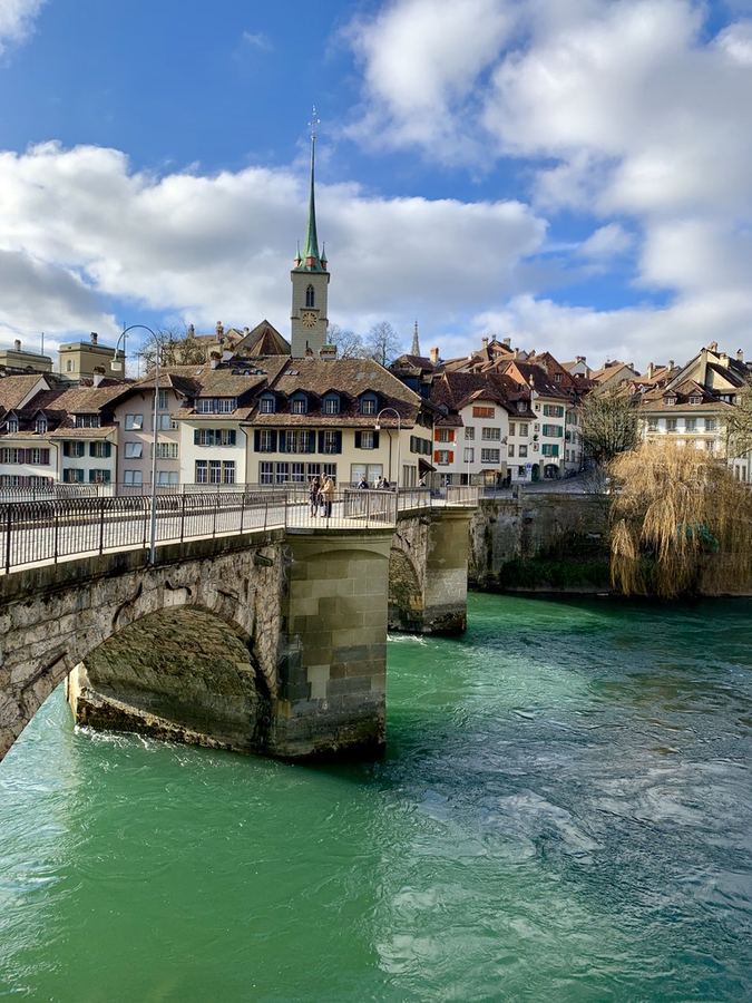 A stone bridge crossing turquoise river water below an old town