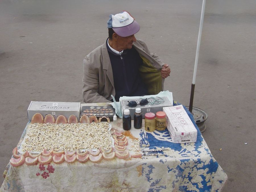 A pavement trader seated behind a cloth spread with shells and small bottles