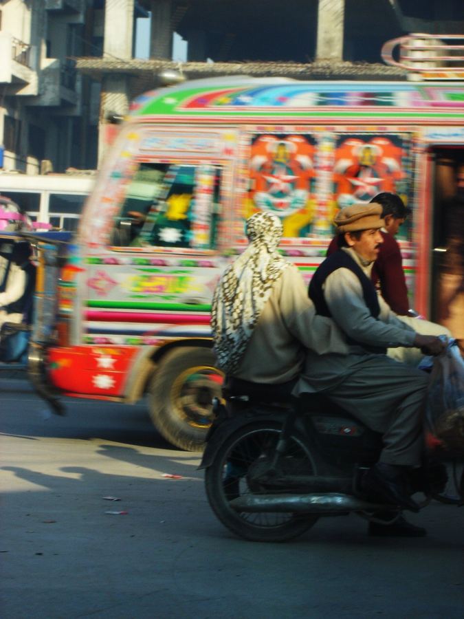 A motorcyclist passing a hand-painted bus in traffic