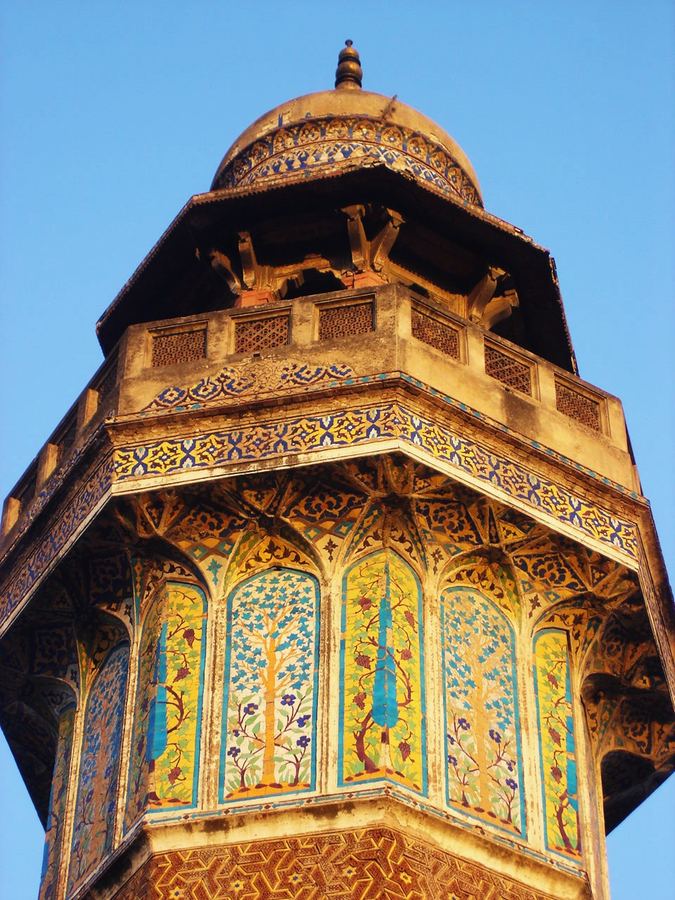 A tiled and gilded minaret seen from below against a clear sky