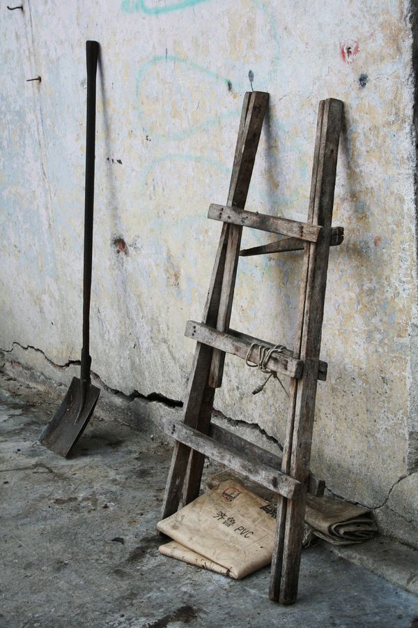 A wooden ladder and shovel leaning against a plaster wall