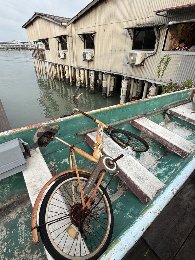 A rusting bicycle leaning against a stilt house above the water