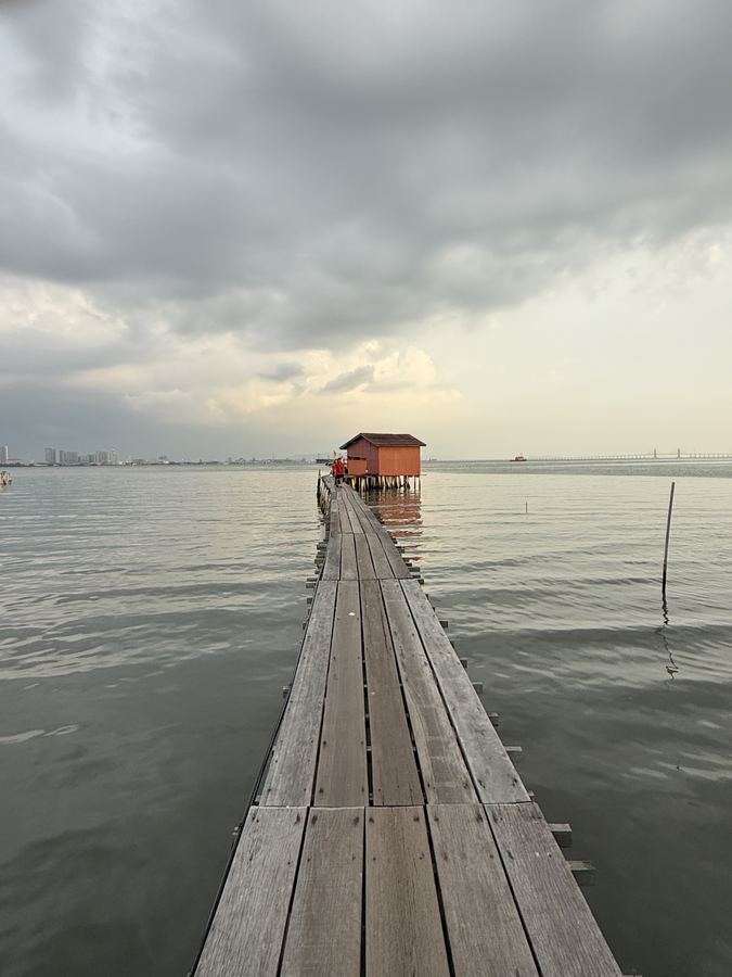 A timber walkway running out to a hut standing in a flat grey sea