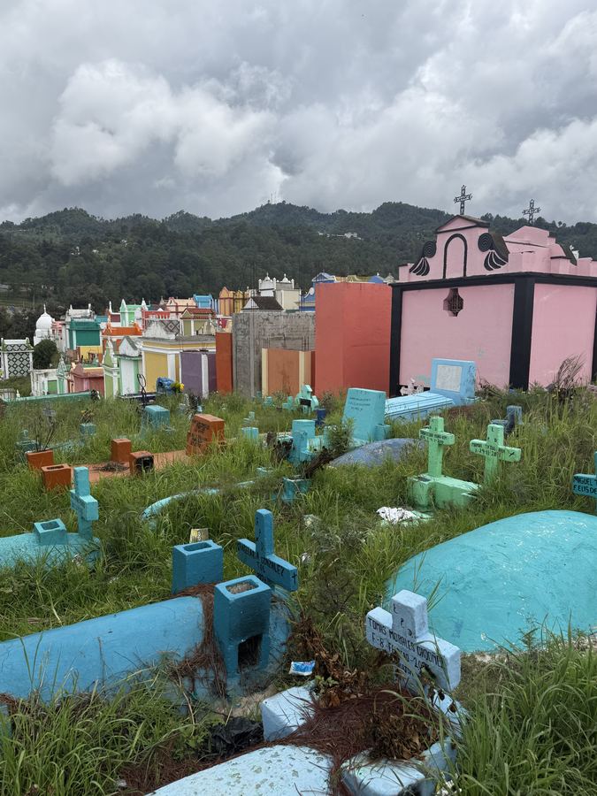 A hillside cemetery of painted tombs and crosses under low cloud