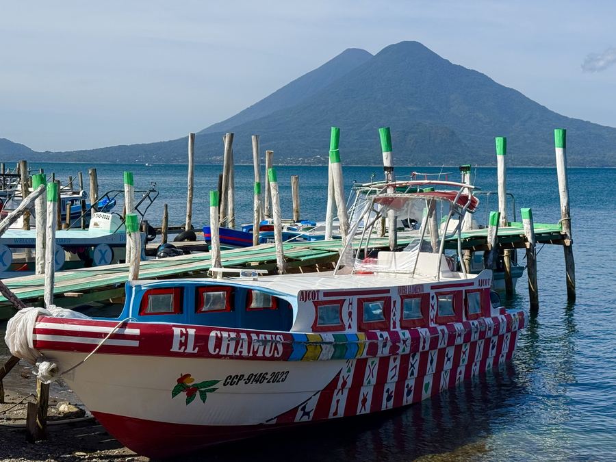 A painted passenger boat moored at a lake dock beneath a volcano