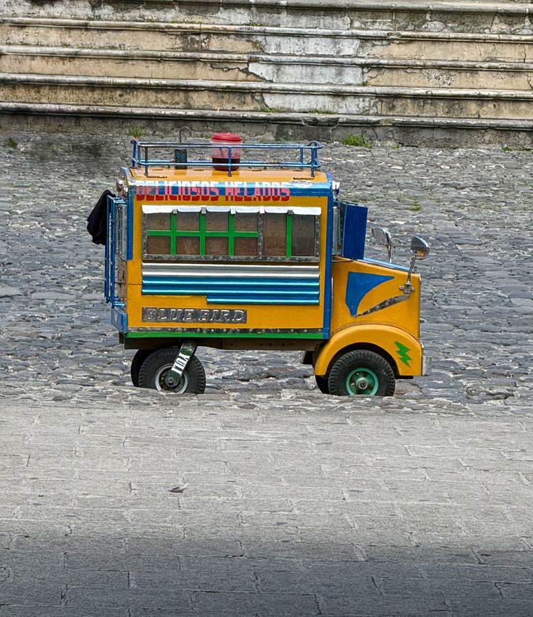 A yellow and blue painted bus parked on cobblestones
