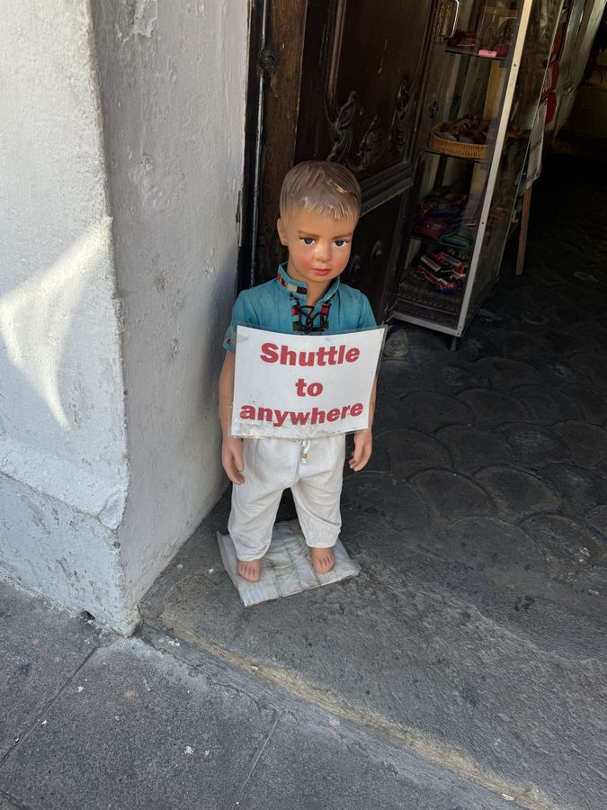 A child mannequin on a shop step holding a sign reading Shuttle to anywhere