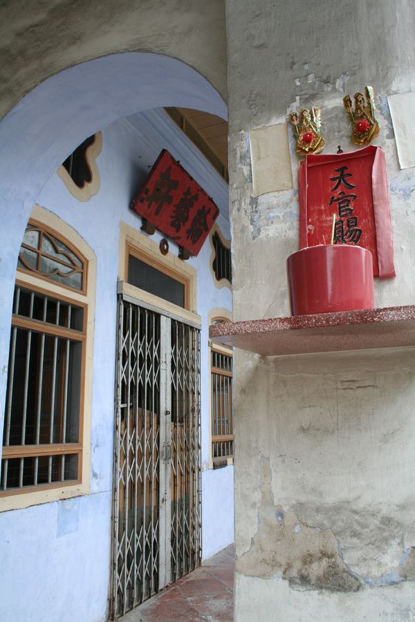 A blue shophouse arcade with red Chinese shrine papers on the pillar
