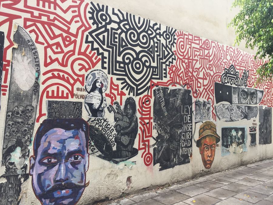 A mural of faces and pattern along a city sidewalk