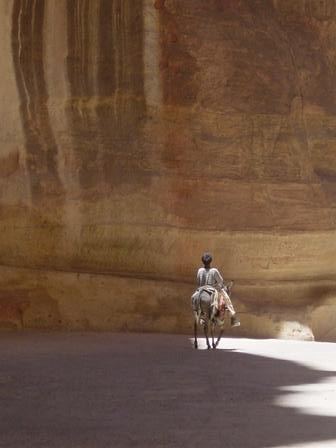 A lone rider on horseback dwarfed by a vast sandstone canyon wall