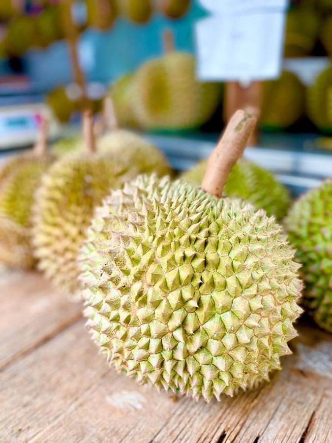 A durian resting on a wooden counter at a fruit stall