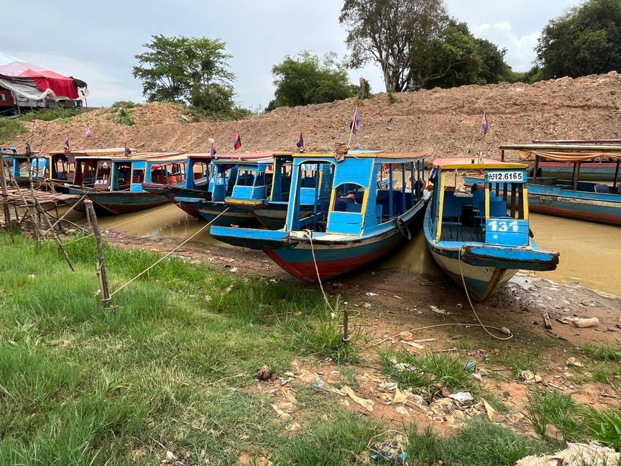 Painted passenger boats moored along a muddy riverbank