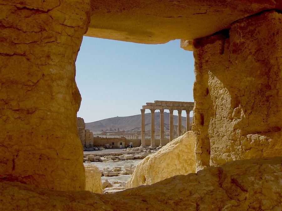 Colonnaded ruins framed through a broken stone window